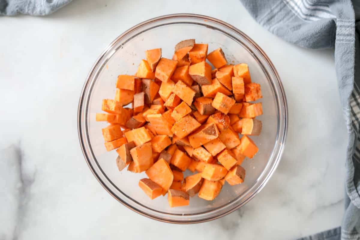 Cubed sweet Potatoes in bowl with seasonings. 