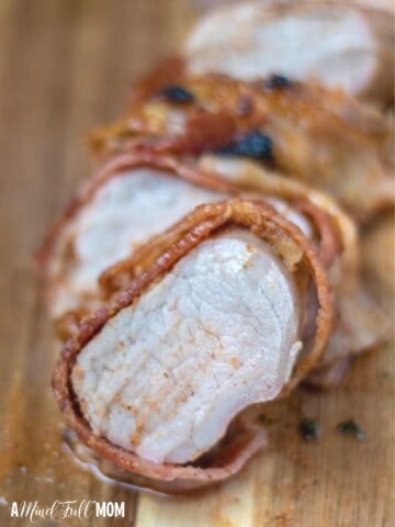 Sliced pork tenderloin wrapped in bacon on cutting board.