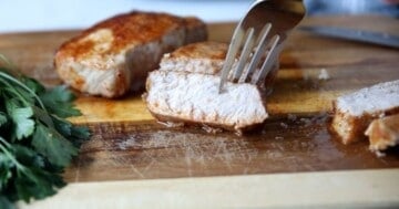 Sliced air fryer pork chops on cutting board with fork grabbing slice.