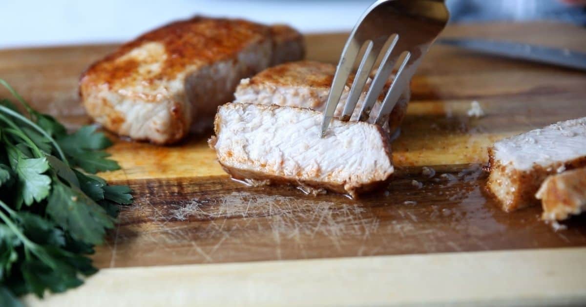Sliced air fryer pork chops on cutting board with fork grabbing slice. 