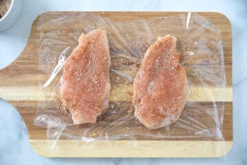 Seasoned chicken breasts on plastic wrap before cooking.