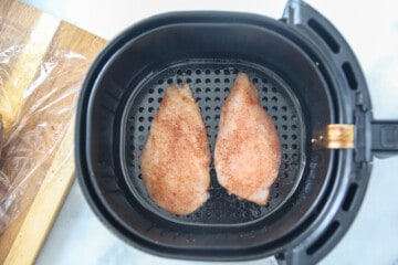2 seasoned chicken breasts in air fryer basket.