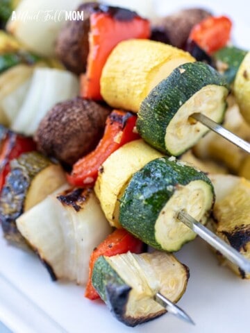 Grilled kabobs with vegetables on white platter.