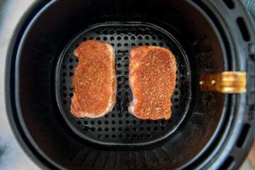 2 seasoned pork chops in air fryer basket.