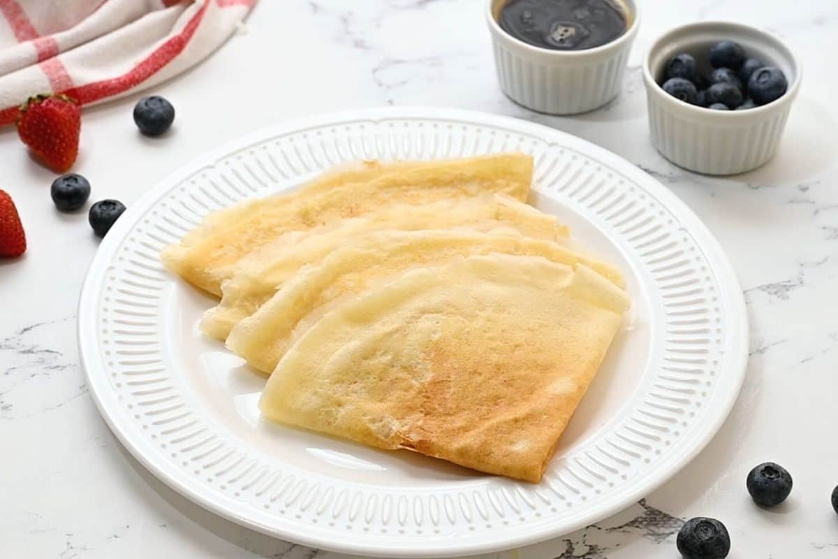 4 folded crepes on a white plate next to maple syrup.