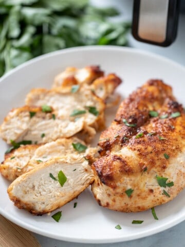 Air Fryer Chicken Breasts on white platter topped with parsley.