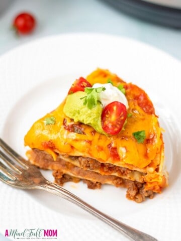 Slice of mexican lasagna on white plate with fork.
