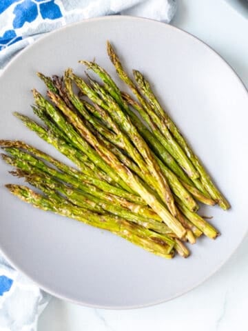 A plate of crispy asparagus next to air fryer.