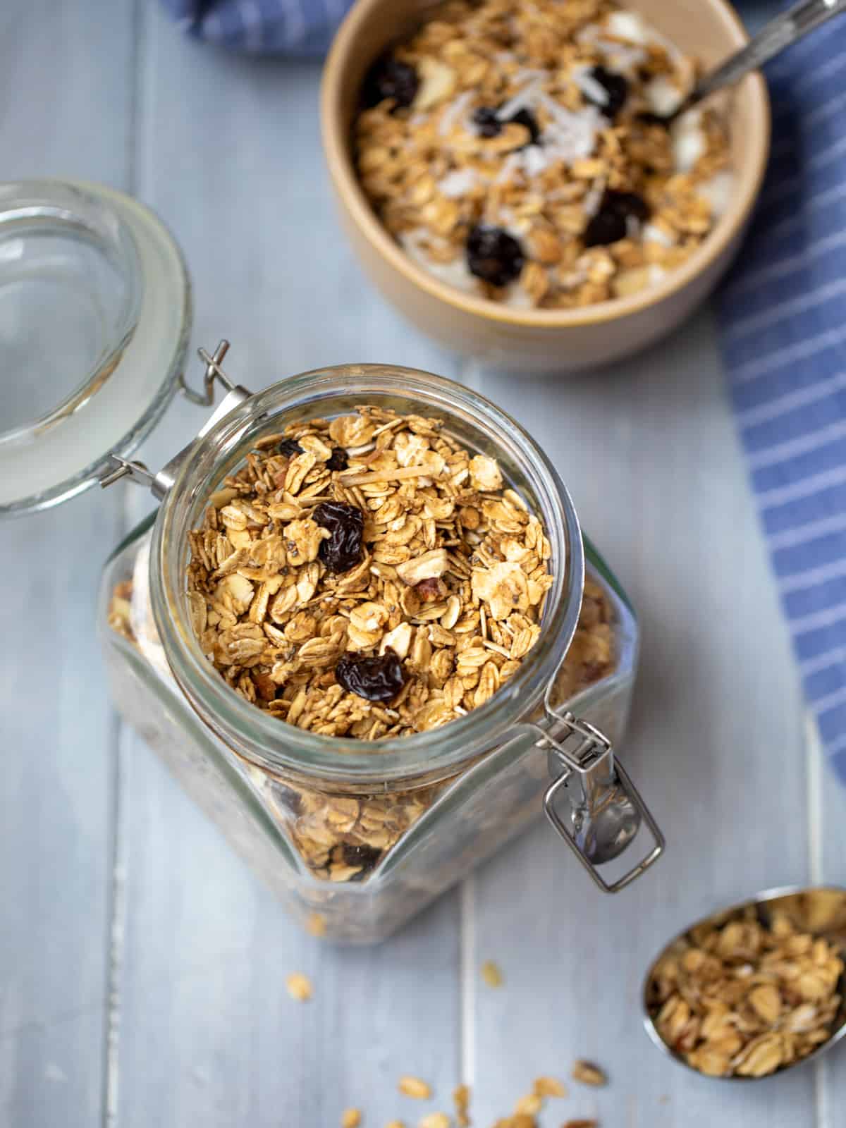 Homemade granola in jar with bowl of granola in background. 