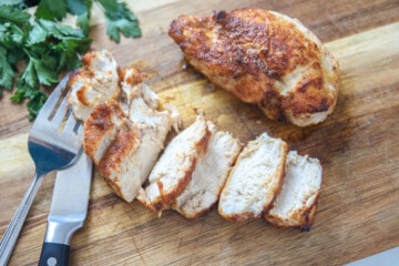 Sliced air fryer chicken breast on wooden cutting board.