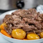 Close up of slow cooker pot roast on white platter with potatoes and carrots.