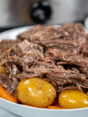 Close up of slow cooker pot roast on white platter with potatoes and carrots.