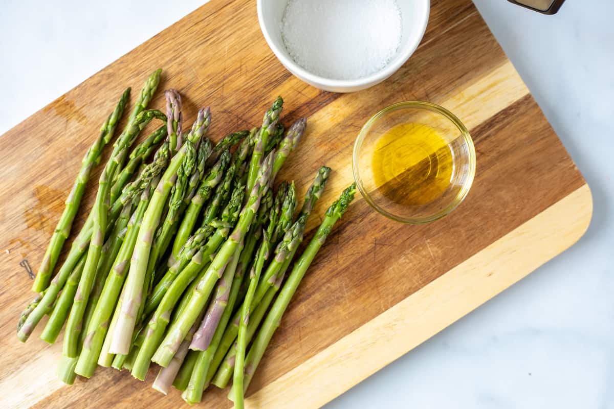 Trimmed asparagus on cutting board next to salt and oil. 