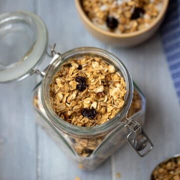 Homemade granola in jar with bowl of granola in background.
