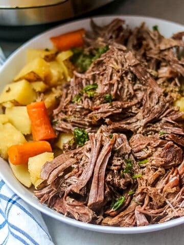 Shredded Pot Roast with carrots and Potatoes in white bowl next to Instant Pot.