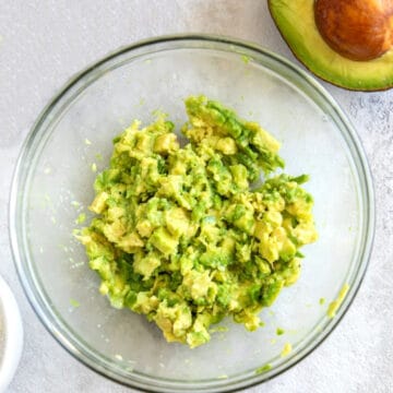 Mashed avocado in bowl with whole avocado next to it.