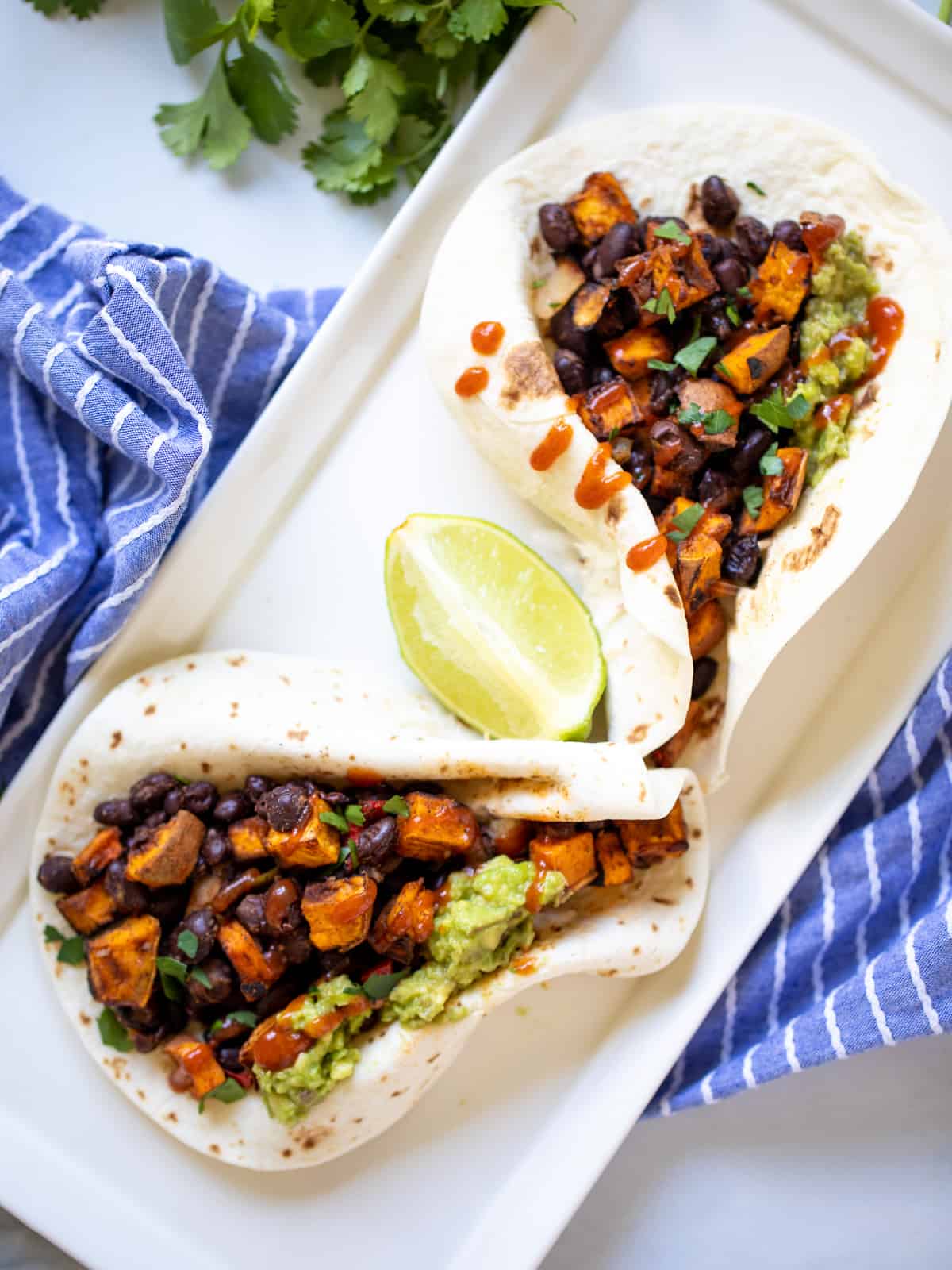 Two flour tortilla filled with sweet potatoes, black beans, and guacamole.