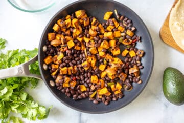 Sauteed cubed sweet potatoes and black beans in saute pan with peppers and onions.