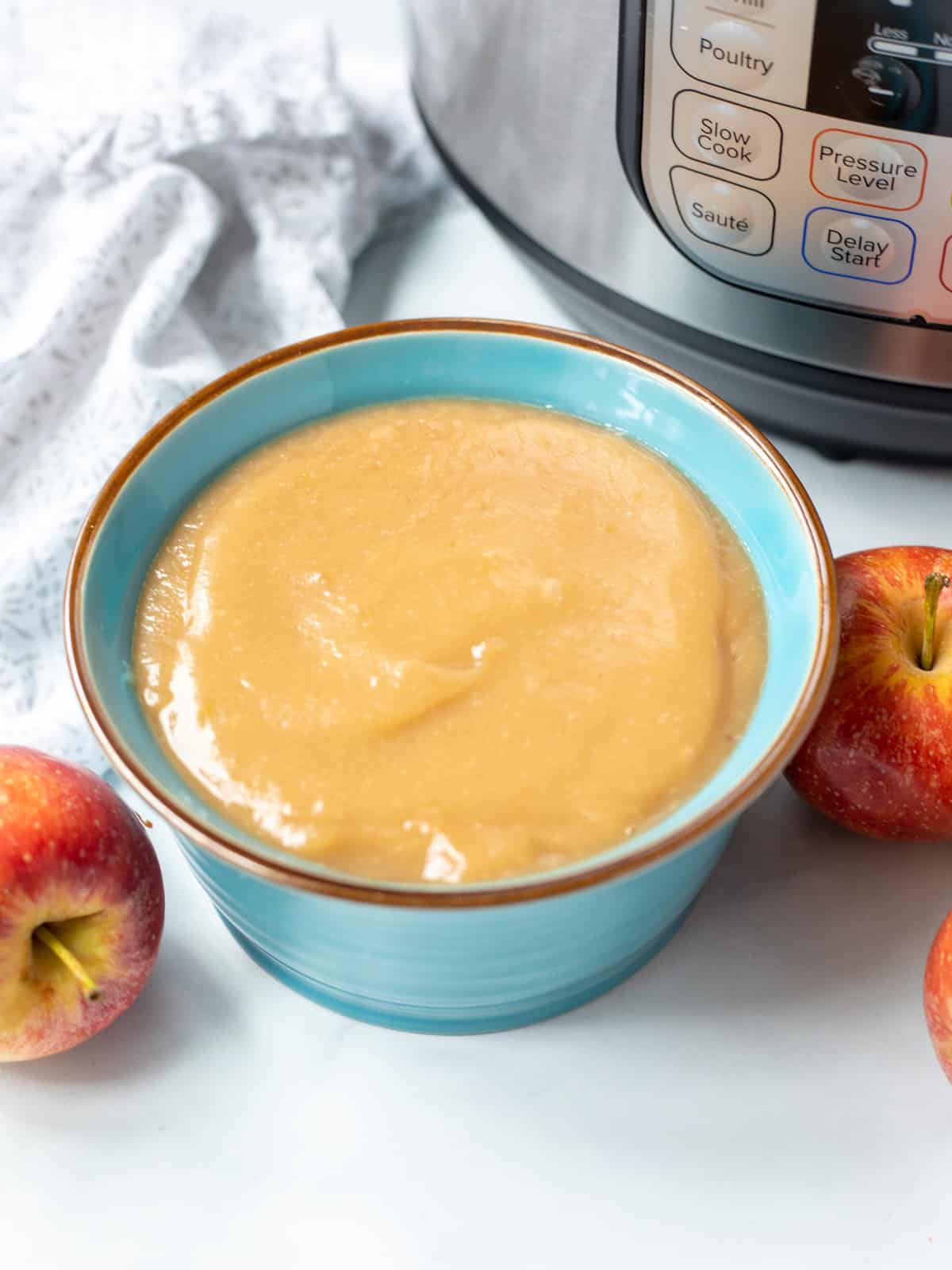 Bowl of homemade applesauce next to apples and instant pot. 