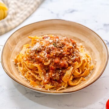 Pasta topped with bolognese sauce on cream plate.