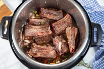 Seared beef short ribs in brasing liquid in inner pot.