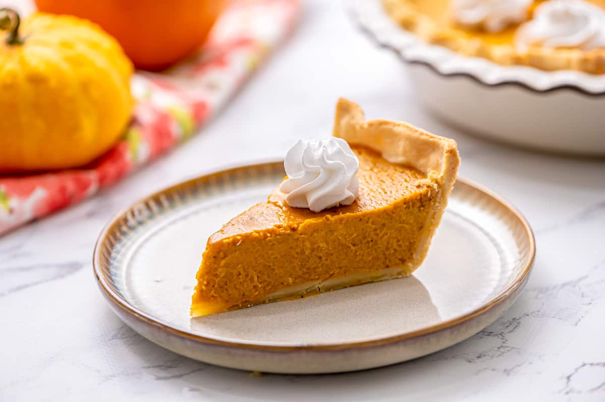 Slice of pumpkin pie on plate toped with whipped cream. 