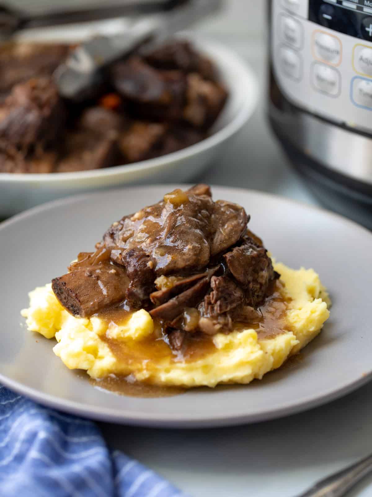 Instant Pot short ribs plated on top of mashed potatoes with Instant Pot in background. 
