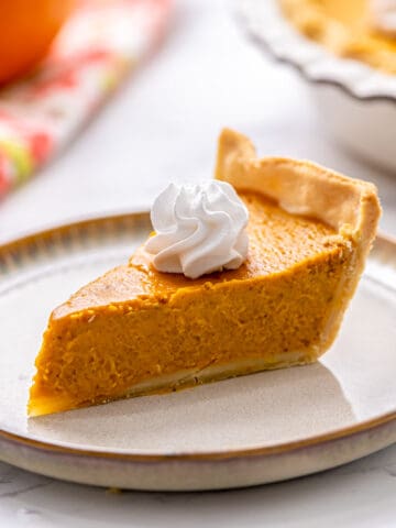 Slice of pumpkin pie on plate toped with whipped cream.