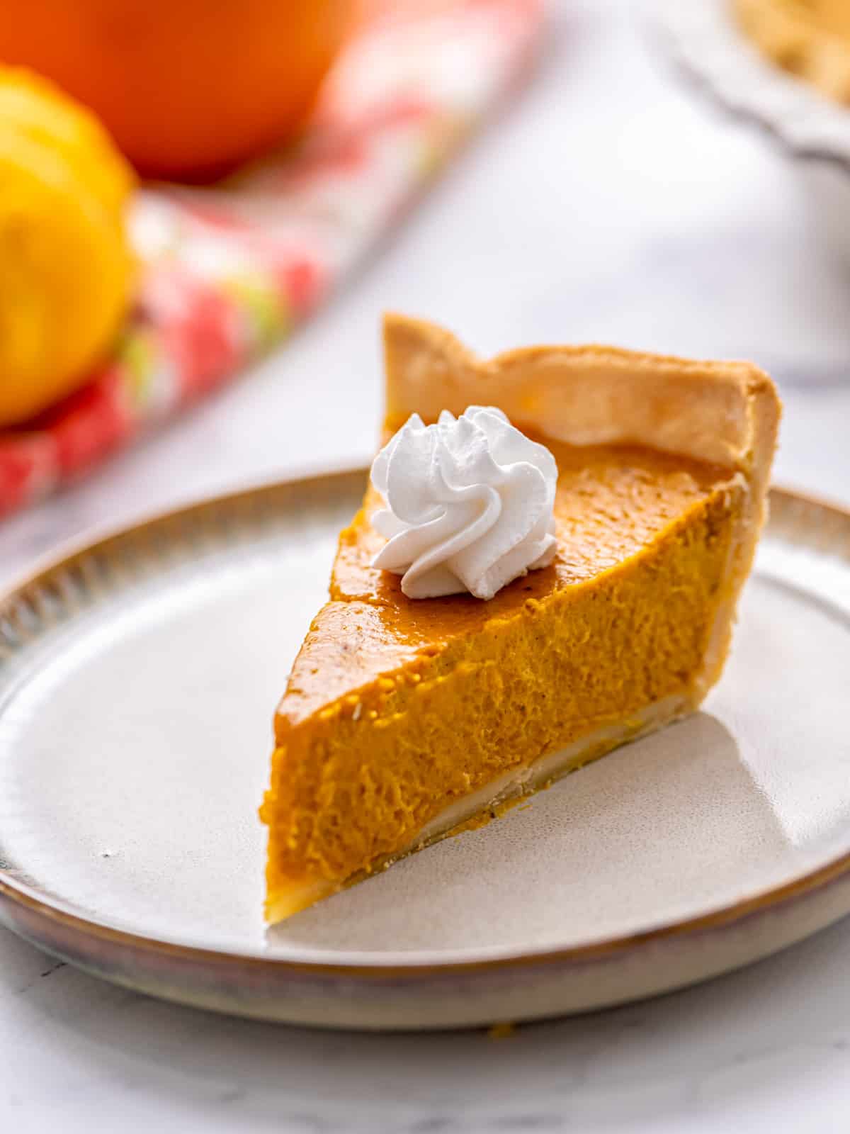 Slice of homemade pumpkin pie on white plate with whipped cream.