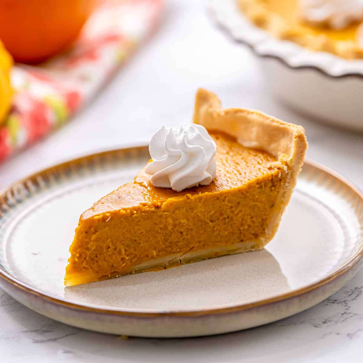 Slice of pumpkin pie on plate toped with whipped cream.