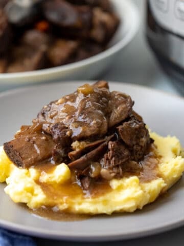 Short Ribs served with braising liquid over mashed potatoes with Instant Pot in the background.