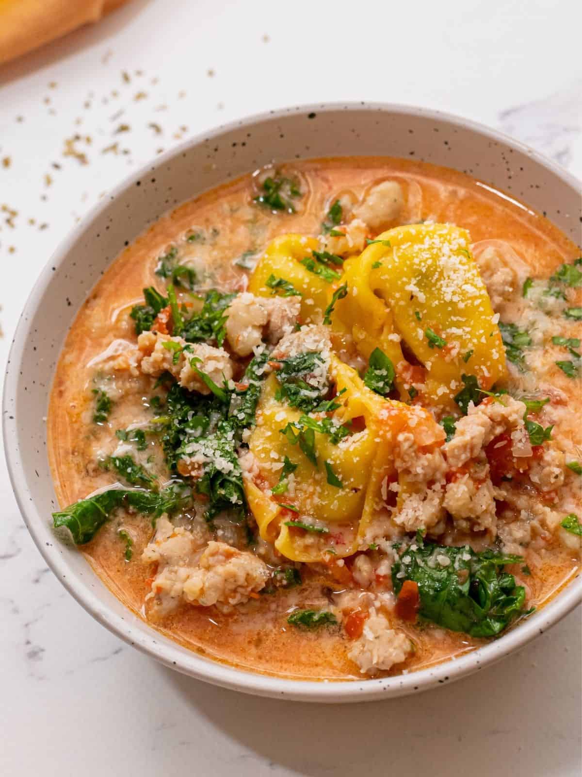 Bowl of tortellini soup with sausage and greens.