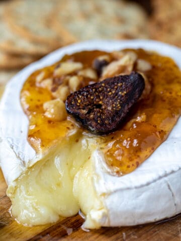 Wheel of brie topped with fig jam with cheese coming out.