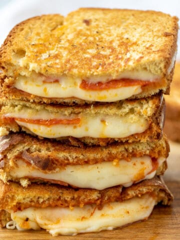 Stack of Pizza Grilled Cheese cut in half showing cheese oozing out on cutting board.