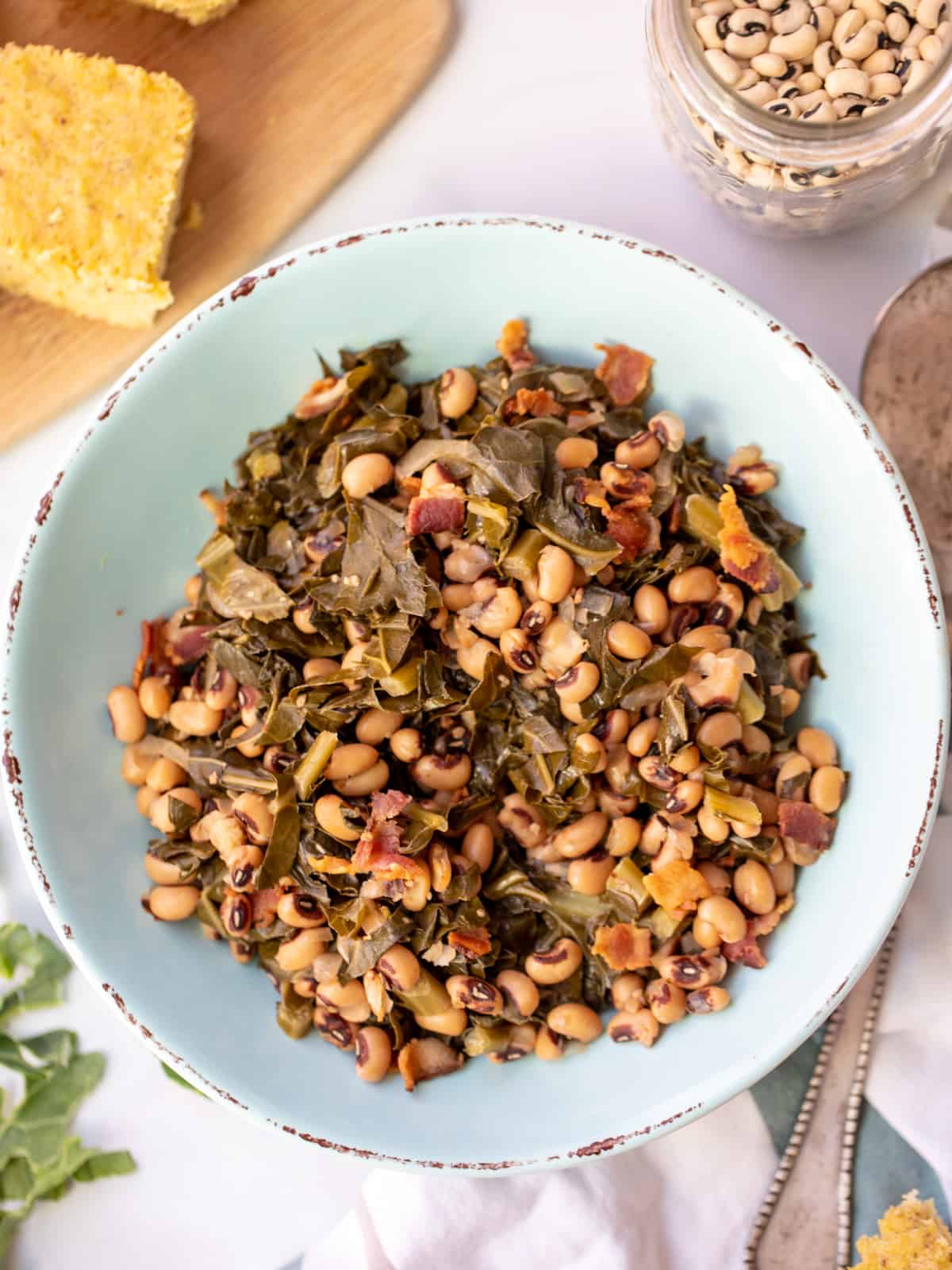 Bowl of Instant Pot Black Eyed Peas and Collard Greens next to cornbread and dried beans. 
