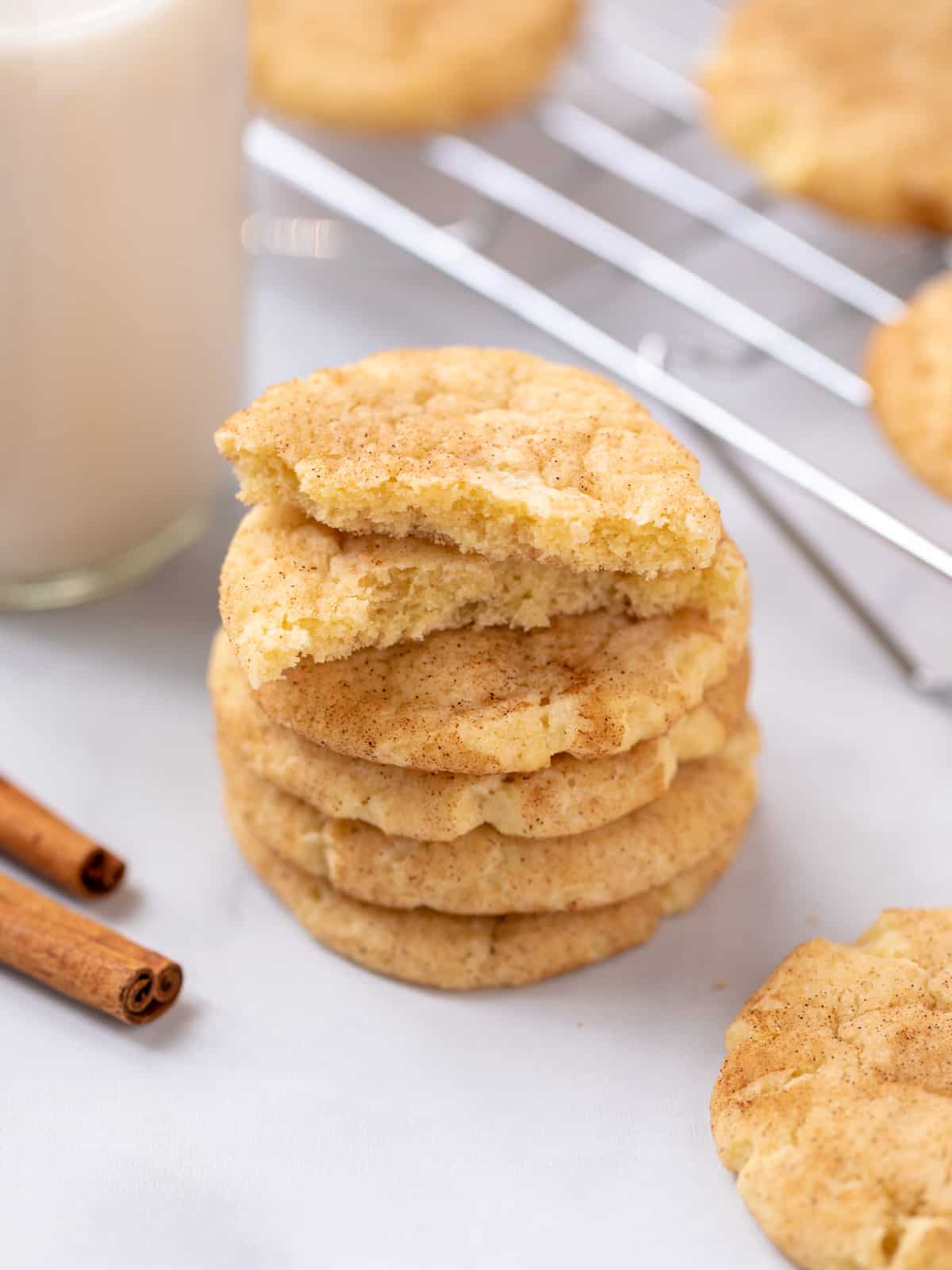 Stack of snickerdoodle cookies next to glass of milk and cinnamon sticks.