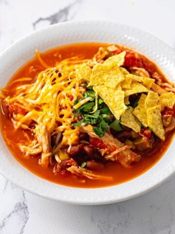 Bowl of chicken chili topped with corn chips and cheese.