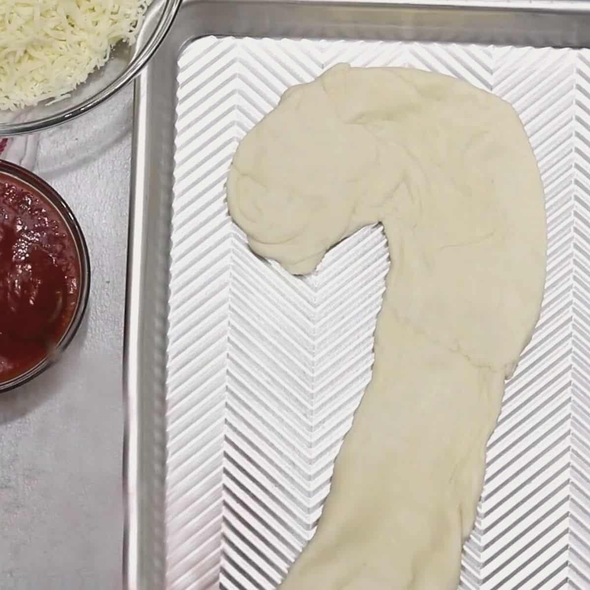 Pizza dough shaped like a candy cane on sheet pan.