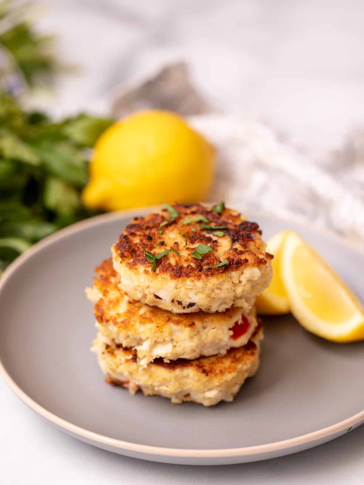 Crab Cakes stacked on top of each other on gray plate with lemon in the background. 