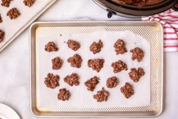 Peanut clusters with chocolate in small mounds on parchment paper on baking tray.