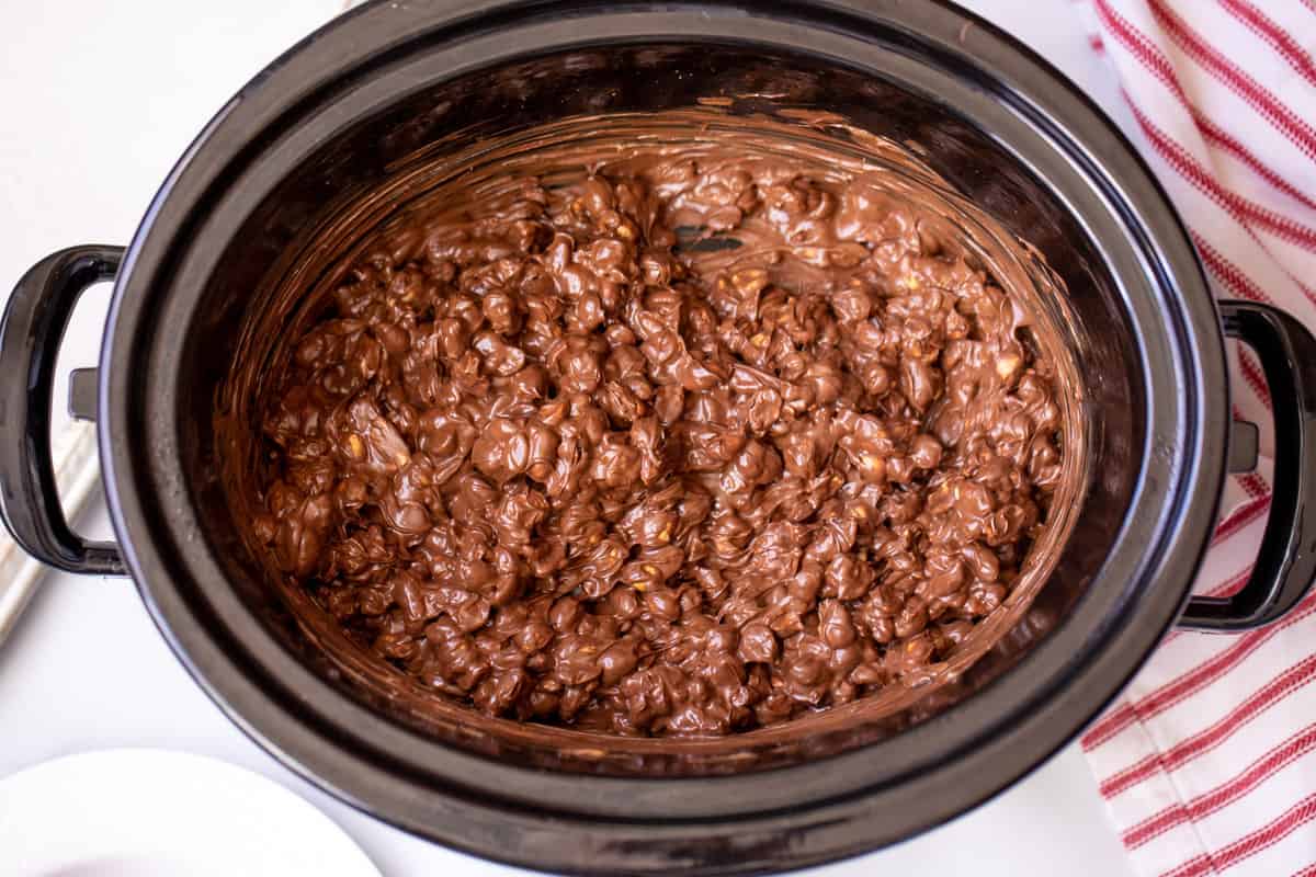 Melted chocolate chips coating peanuts in a slow cooker.