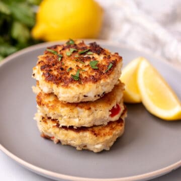 Crab Cakes stacked on top of each other on gray plate with lemon in the background.