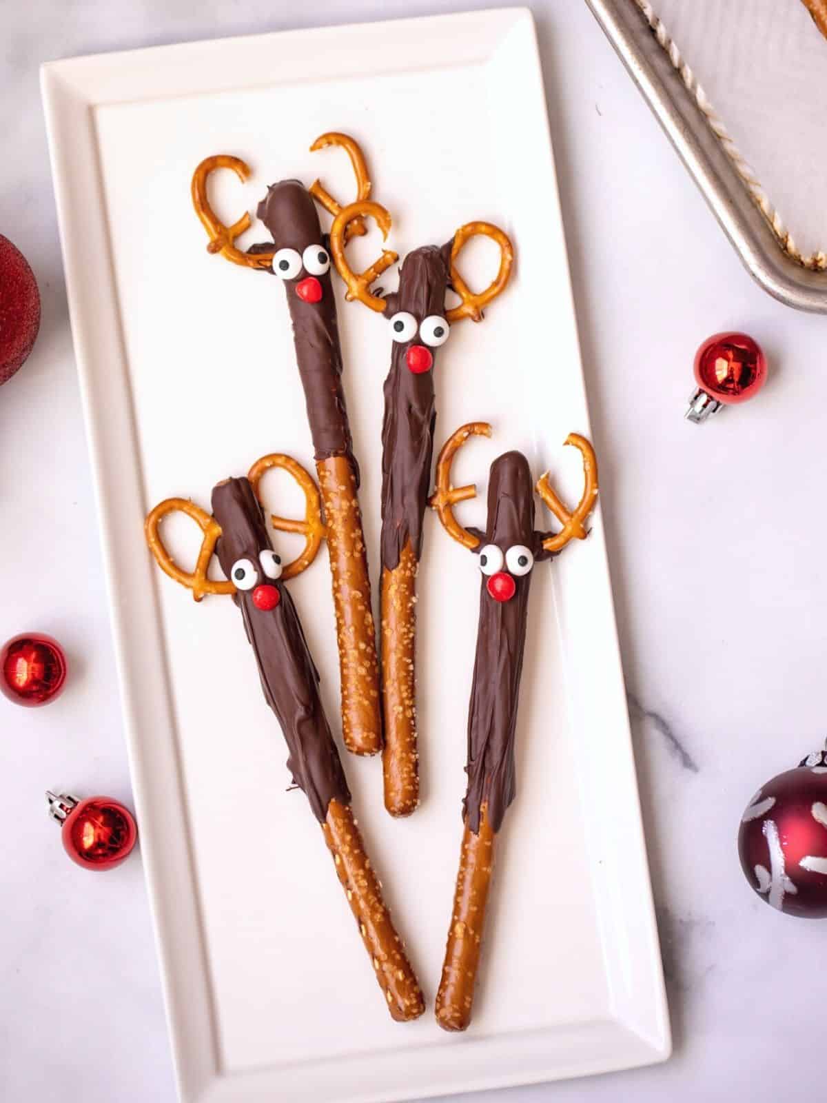 4 chocolate covered pretzels decorated to look like Rudolph on a white platter. 