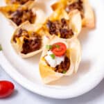 Wonton Taco Cups on white platter topped with tomatoes and sour cream.
