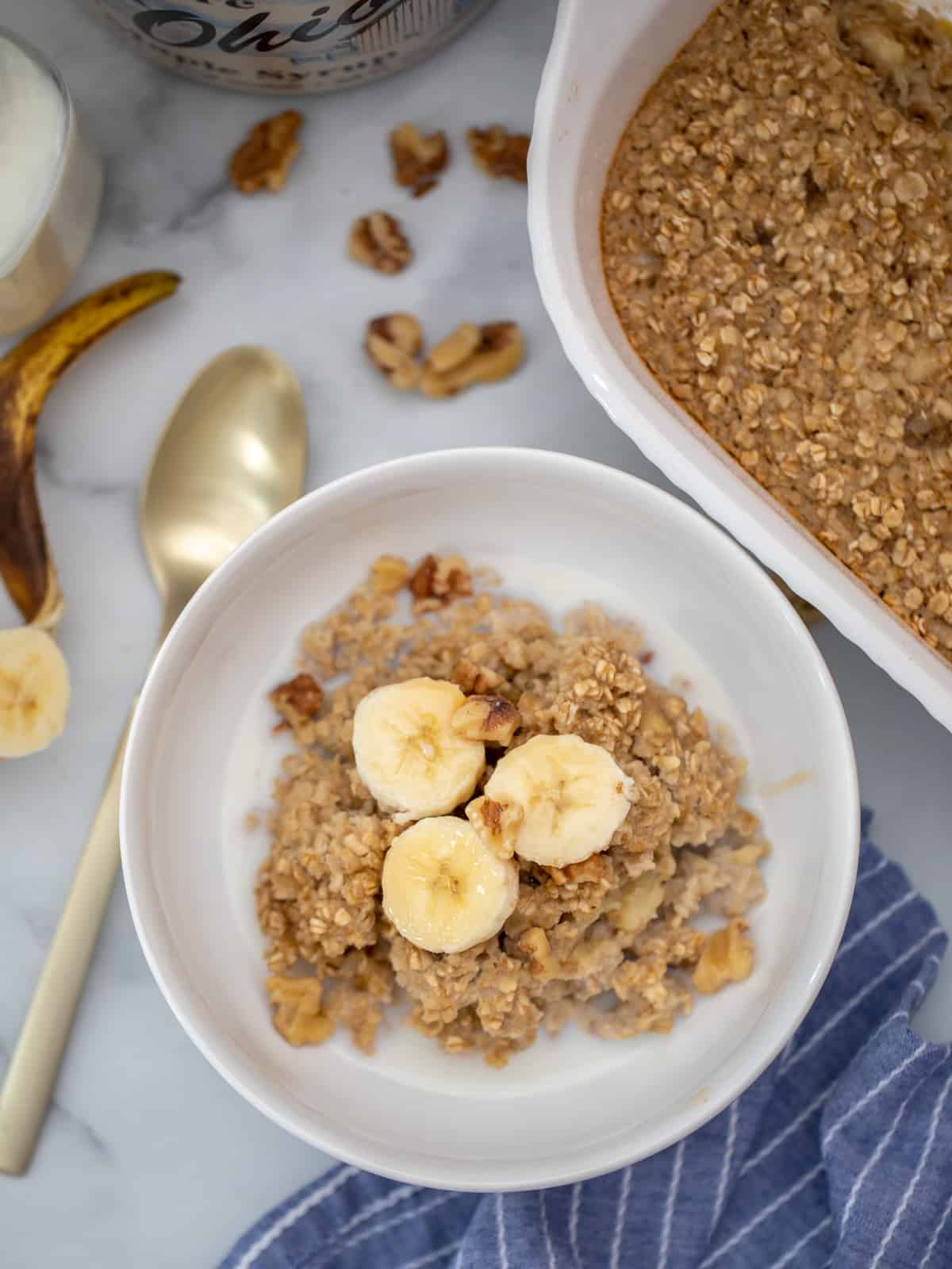 Bowl of banana baked oatmeal topped with banana slices and walnuts with baked oatmeal off to the side. 