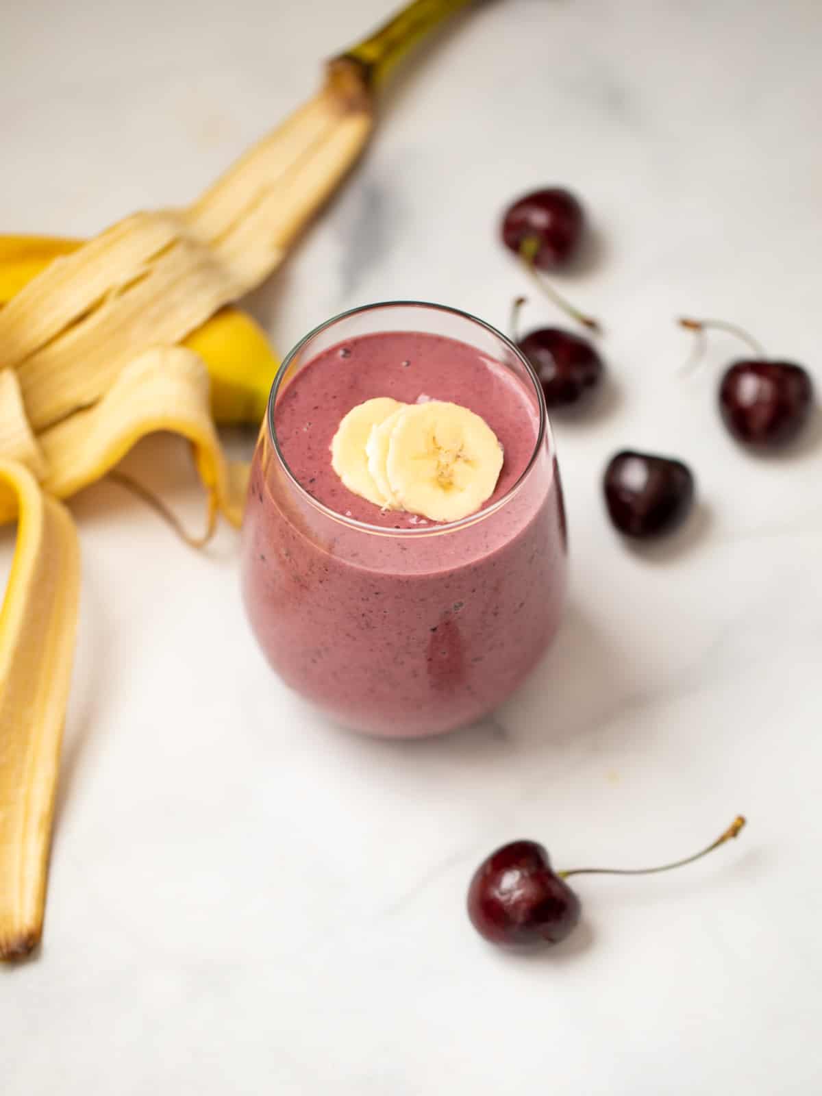 Cherry Smoothie in clear glass next to fresh cherries and banana. 