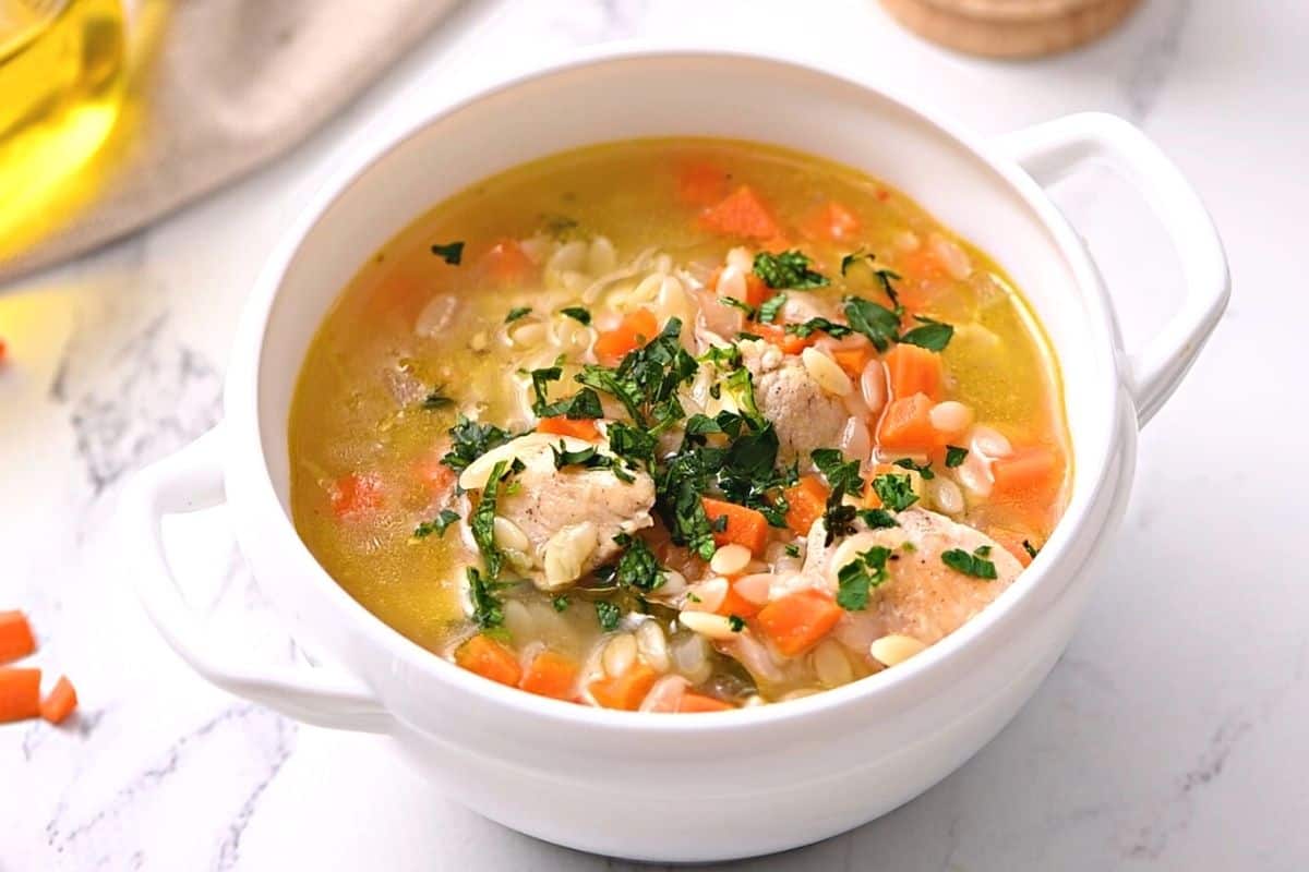 Orzo Soup in white bowl topped with fresh parsley.