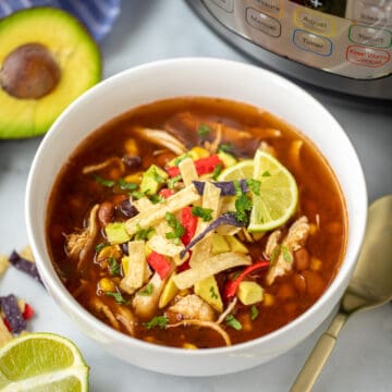 Bowl of Instant Pot Chicken Tortilla Soup topped with avocado, lime, and tortilla strips.