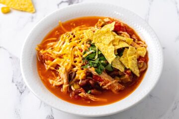 Bowl of chicken chili in white bowl topped with shredded cheese and chops.