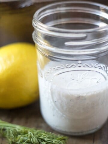 Jar of homemade ranch dressing next to dill and lemon.